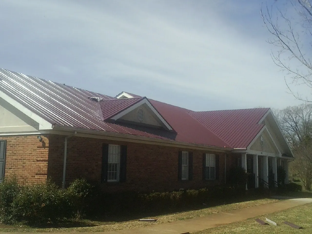 Red metal roof with gabled entries on a long brick building, from a Hail Damage Roof Repair job in Sharpsburg